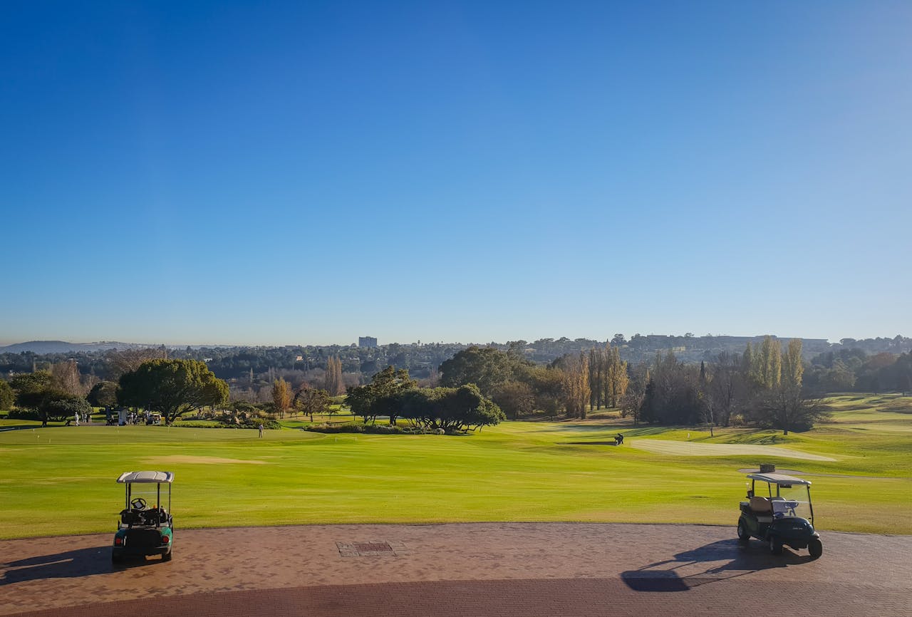 A panoramic view of a golf course with golf carts under a clear blue sky on a sunny day.